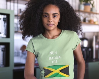Può includere: Una maglietta verde chiaro con il testo "NUH BADDA MI" e una grafica della bandiera giamaicana.