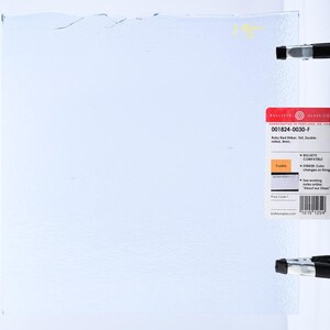May include: A sheet of light blue glass with a textured surface, held in place by black clamps. A red and white label on the right side provides product information, including the text "Ruby Red Striker, Tint, Double-rolled, 3mm."