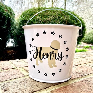 May include: White metal bucket with a black paw print design and the name "Henry" in black script. A gold silhouette of a dog is in the center of the bucket.