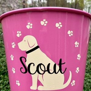 May include: Pink metal dog treat bucket with a white dog silhouette and the name "Scout" in black lettering. The bucket is decorated with white paw prints.