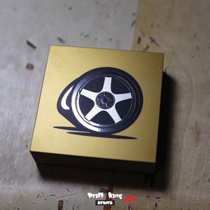 May include: A gold box with a black and white illustration of a car wheel. The box has the text "Drift King Series #1" printed on the bottom.