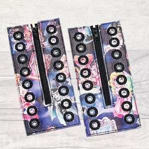 May include: Two black fabric zippered pouches with a colourful print of a starry night sky and cartoon characters. Each pouch has multiple rows of black eyelets.