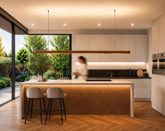 May include: Modern kitchen with a large island, two bar stools, and a wooden light fixture. The kitchen features white cabinets, a black countertop, and a large window overlooking a lush green yard. The floor is made of wood.