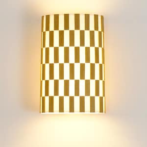 Op de afbeelding: Een wandlamp met een cilindrische kap met een geruit patroon in wit en bruin.
