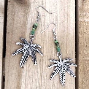 Op de afbeelding: Zilveren marihuana-blaadjes oorbellen met groene kralen.