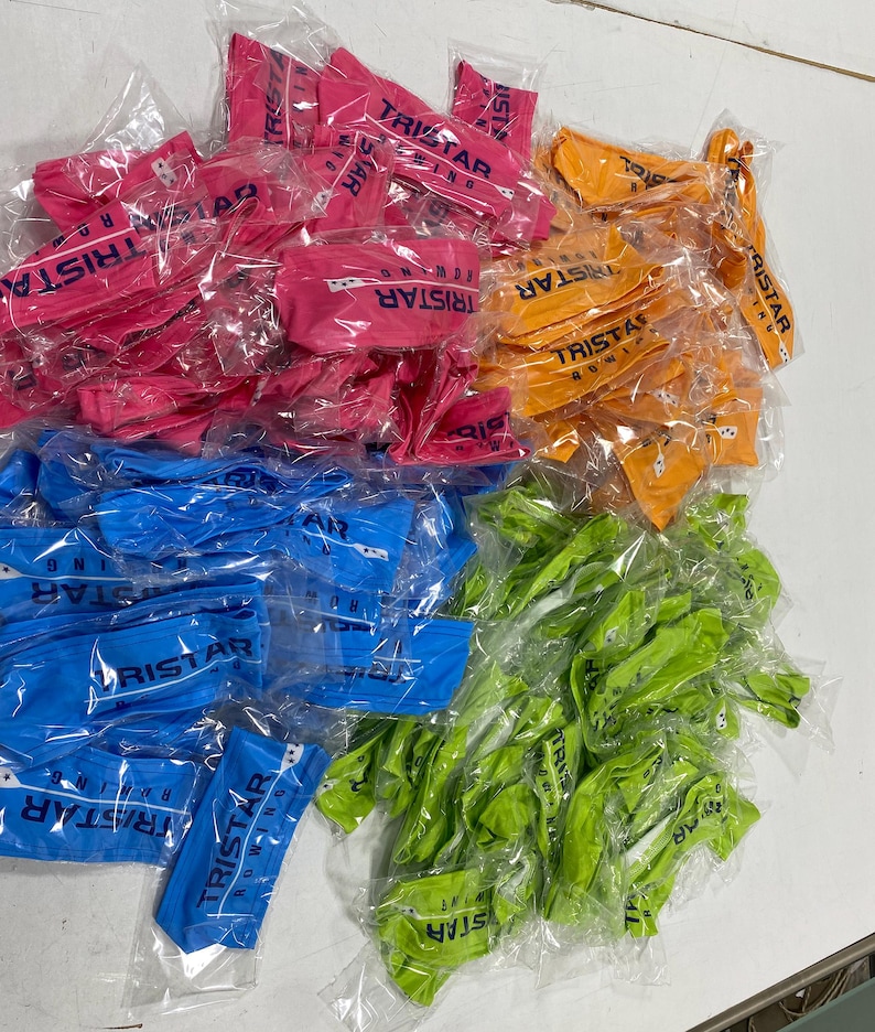 May include: A large pile of colorful headbands with the logo "TRISTAR RUNNING" printed on them. The headbands are packaged individually in clear plastic bags.