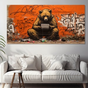 Puede incluir: Un oso marrón sentado en una pared naranja brillante con grafiti. El oso sostiene una tableta en sus patas. El grafiti incluye las palabras "The Bad" y "Too Much".