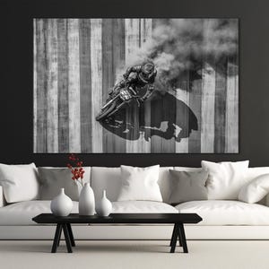 Pu&ograve; includere: Fotografia in bianco e nero di un motociclista in curva, che crea una nuvola di fumo. Lo sfondo presenta strisce verticali in tonalit&agrave; di grigio e bianco. Il pilota indossa un casco e un'attrezzatura protettiva.
