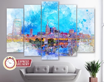 Op de afbeelding: Een aquarel schilderij van de skyline van Nashville 's nachts. De stad is verlicht met lichten, en de rivier reflecteert de lichten. Het schilderij is verdeeld in vijf panelen.