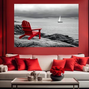 May include: A red Adirondack chair sits on a rocky shore overlooking a black and white seascape with a sailboat in the distance.