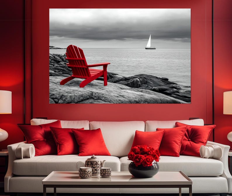 May include: A red Adirondack chair sits on a rocky shore overlooking a black and white seascape with a sailboat in the distance.