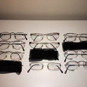 May include: A collection of ten pairs of eyeglasses with various frame styles and colors, including black, gold, and silver. The frames are all made of metal and have clear lenses. The brand name "Carrera" is visible on the arms of some of the frames.