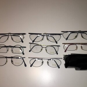 Puede incluir: Una colección de ocho pares de gafas negras, doradas y plateadas con el nombre de la marca "TAHRI" impreso en las monturas.