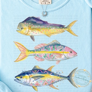 May include: A pale blue sweatshirt displaying three vibrantly coloured fish designs. The fish are depicted in yellow, pink, blue, and purple, with detailed patterns. The design includes the text "ORIGINAL DESIGN DO NOT COPY Sunshine & Razberry".