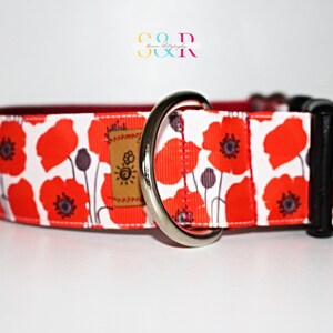 May include: A white dog collar with a red poppy print and a silver D-ring. The collar has a black buckle.