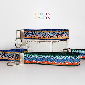 May include: Keychains with a colorful pattern resembling fish scales. The keychains have a blue background with orange, brown, and blue spots. The keychains have metal hardware and key rings. The keychains are displayed on a white surface.