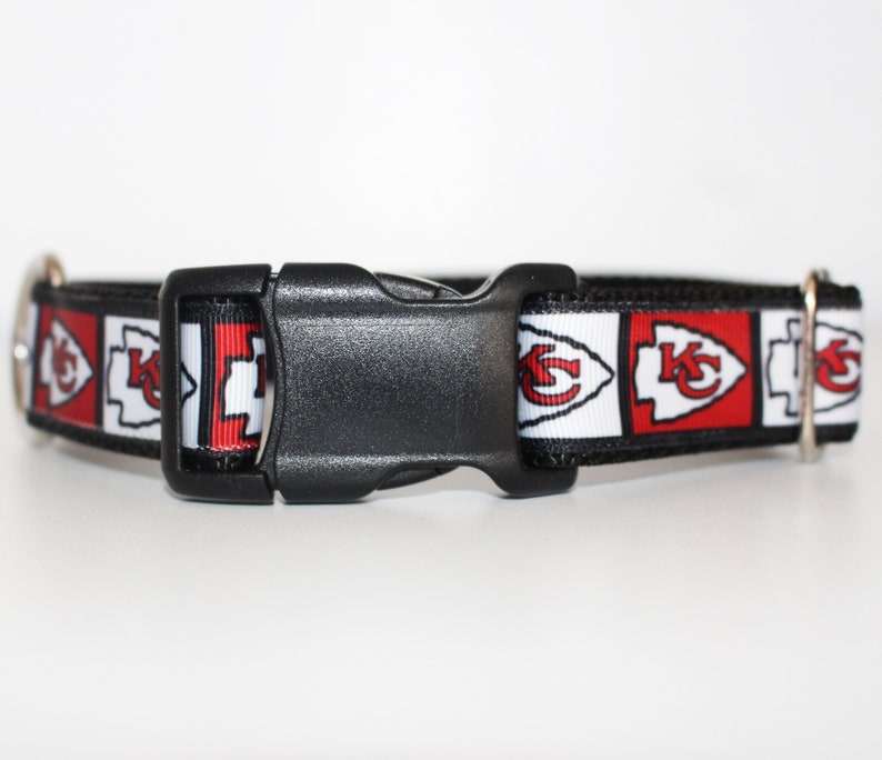 Peut inclure: Un collier de chien noir avec un ruban &agrave; motif rouge, blanc et noir repr&eacute;sentant le logo des Kansas City Chiefs. Le collier a une boucle en plastique noire.