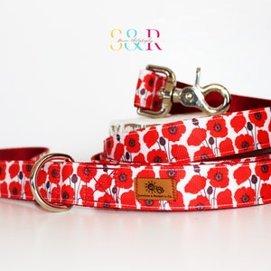 May include: Red and white dog leash and collar set with a poppy flower print. The leash has a silver D-ring and the collar has a silver clip. The set is made by Sunshine & Battery Co.