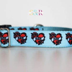 May include: A light blue dog collar with a repeating pattern of red hearts with black outlines and the word "MOM" inside each heart. The hearts are surrounded by black floral designs.