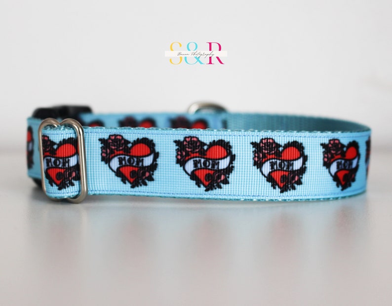 May include: A light blue dog collar with a repeating pattern of red hearts with black outlines and the word "MOM" inside each heart. The hearts are surrounded by black floral designs.