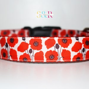 May include: A white dog collar with a red poppy floral print. The collar has a black plastic buckle.