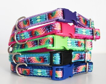 May include: A stack of five colorful tie-dye dog collars with silver D-rings and plastic buckles. The collars are in shades of purple, pink, green, blue, and teal.