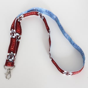 May include: A lanyard with a silver clasp. The lanyard is patterned with the words "Chiefs" in white on a maroon background. The other side of the lanyard is light blue with the words "KC Royals" in white.