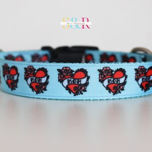 May include: A light blue dog collar with a repeating pattern of red hearts with black outlines and the word "MOM" inside. The hearts are surrounded by black floral designs.