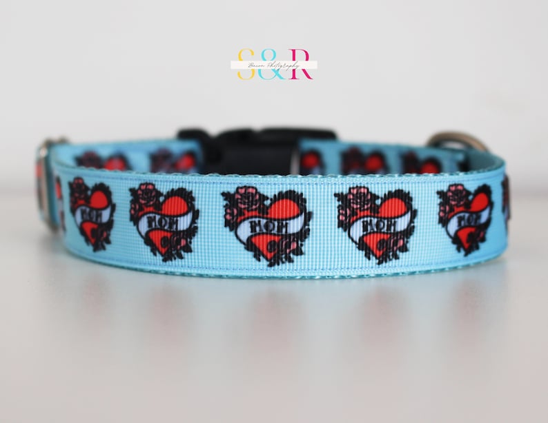 May include: A light blue dog collar with a repeating pattern of red hearts with black outlines and the word "MOM" inside. The hearts are surrounded by black floral designs.