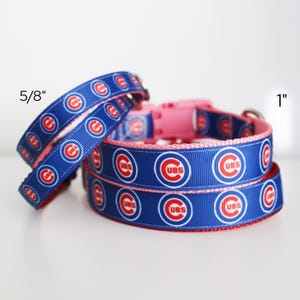 May include: Blue dog collars with the Chicago Cubs logo in red and white. The collars are available in 5/8 inch and 1 inch widths. The collars have a pink buckle.
