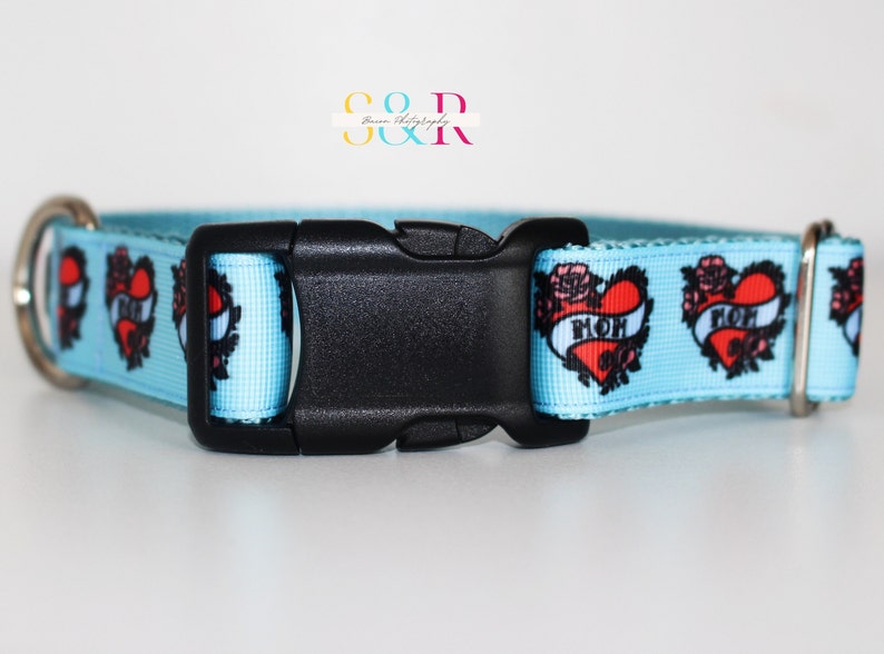 May include: A light blue dog collar with a black buckle. The collar has a repeating pattern of red hearts with black outlines and the word "MOM" inside each heart. The hearts are surrounded by black roses.