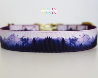 May include: A dog collar with a landscape design featuring mountains and trees in shades of purple and blue. The collar has a gold-colored buckle and a dark purple interior.