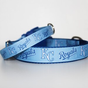 May include: Two light blue dog collars with a white "KC Royals" logo and blue lettering. The collars are made of a soft, durable material and are perfect for any Royals fan.