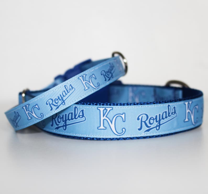 May include: Two light blue dog collars with a white "KC Royals" logo and blue lettering. The collars are made of a soft, durable material and are perfect for any Royals fan.