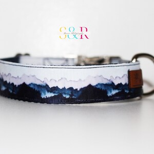 K&ouml;nnte beinhalten: Ein wei&szlig;es Hundehalsband mit einem blauen und violetten Bergdruck. Das Halsband hat eine silberne Schnalle und einen braunen Lederfleck.