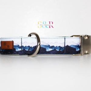 K&ouml;nnte beinhalten: Ein wei&szlig;-blaues Hundehalsband mit einem Bergpanorama-Design. Das Halsband hat eine silberne Schnalle und einen silbernen D-Ring. Das Halsband ist aus strapazierf&auml;higem Nylon.