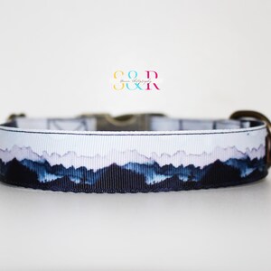 K&ouml;nnte beinhalten: Ein wei&szlig;-blaues Hundehalsband mit einem Bergpanorama-Design. Das Halsband hat eine Messing-Schnalle und einen D-Ring.