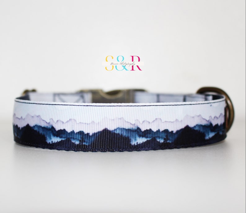 K&ouml;nnte beinhalten: Ein wei&szlig;-blaues Hundehalsband mit einem Bergpanorama-Design. Das Halsband hat eine Messing-Schnalle und einen D-Ring.