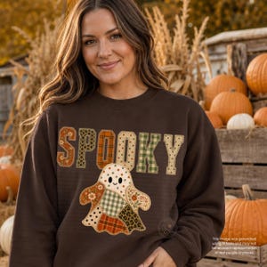 May include: A dark brown long-sleeve sweatshirt featuring the word SPOOKY in large, multi-patterned fabric letters. Below the text is a ghost graphic composed of various patchwork fabric designs including floral, plaid, and polka dot patterns.