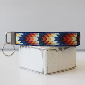 May include: A blue and orange patterned key chain with a silver key ring. The key chain is made of fabric and has a geometric design.