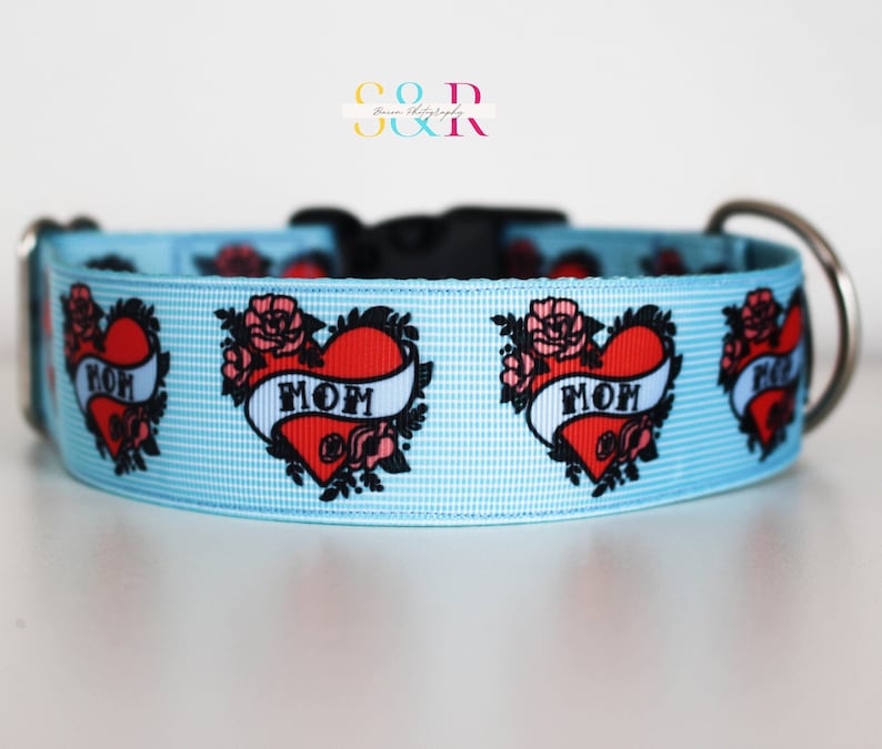 May include: Light blue dog collar with a repeating pattern of red hearts with black outlines and the word "MOM" in a banner. The hearts are surrounded by black floral designs.