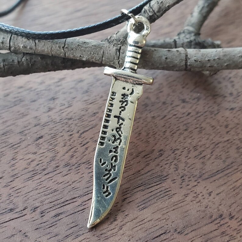 May include: Silver sword pendant necklace with a black cord. The sword has Japanese text engraved on it.