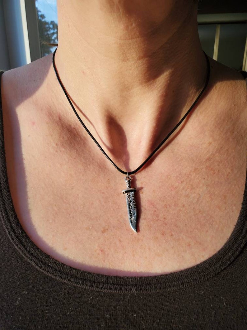 May include: A black cord necklace with a silver knife pendant. The knife has a detailed design and a sharp point.