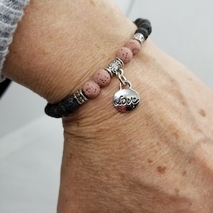 May include: A black and pink lava rock bracelet with a silver charm that says "Love".