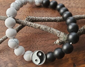 May include: A black and white beaded bracelet with a yin yang charm. The bracelet is made of black and white beads and has a silver yin yang charm in the center.