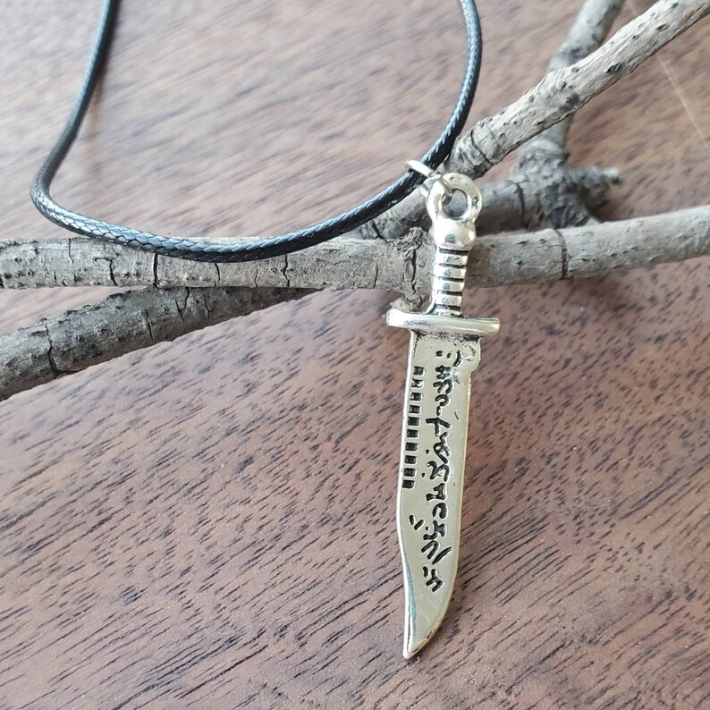 May include: A silver sword pendant necklace with a black leather cord. The sword has an inscription in Japanese characters.