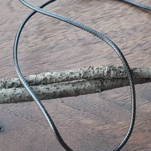 May include: A close-up of black braided cord, with a textured surface, lying on a wooden surface.