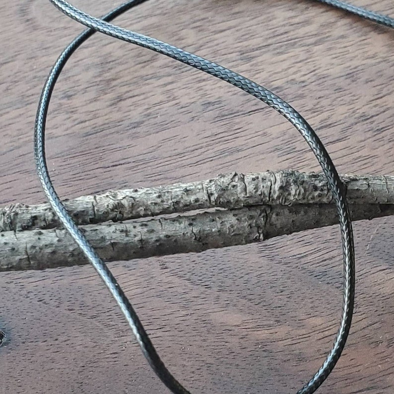 May include: A close-up of black braided cord, with a textured surface, lying on a wooden surface.