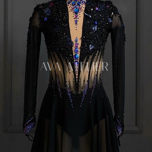Könnte beinhalten: Schwarzes Eiskleid mit langen Ärmeln und hohem Ausschnitt. Das Oberteil ist mit Pailletten und Strasssteinen in Blau- und Lilatönen verziert. Der Rock ist kurz und mehrlagig. Der Text "AVA ATELIER" ist auf dem Kleid zu sehen.
