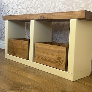 May include: A wooden bench with two storage boxes. The bench is painted white and the boxes are stained brown. The bench is sitting on a wooden floor.